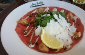 a photo of thin sliced beef capriccio served with fresh arugula and parmesan cheese and capers